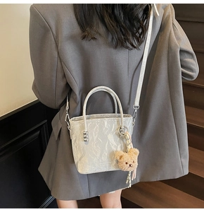 Detail of light gray wrinkled texture bucket bag with a cute plush bear charm