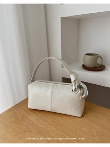 Detail of a minimalist cream shoulder bag with chunky silver chain hardware on a table