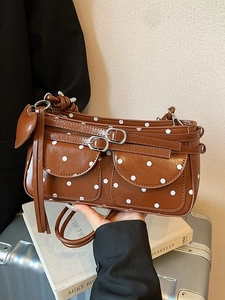 Brown leather underarm bag with white polka dots, twin front pockets, and heart tassels