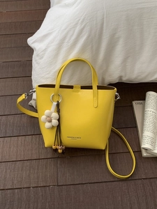 Elegante borsa a secchiello in pelle giallo acceso con manici e ciondolo floreale