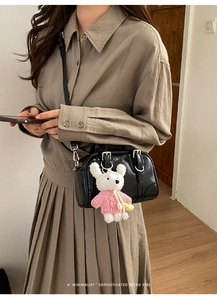 Detail of black glossy square bag with a cute plush rabbit charm and slim leather strap