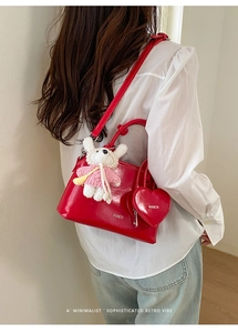 Red glossy shell bag with rabbit charm and heart pouch shown on model in side view