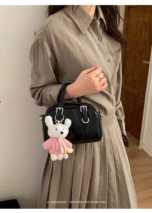Detail of a minimalist black shiny bowling bag featuring a cute plush bear charm with pink sweater