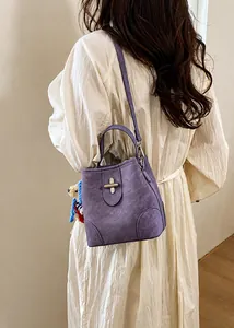 Detail of purple bucket bag with golden cross buckle and cute teddy bear charm