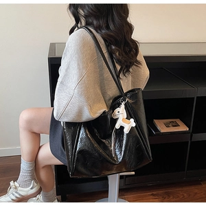 Detail of a large black glossy tote bag with crinkled texture and white horse charm