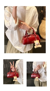 Detail of red patent leather cylindrical handbag with golden zipper and plush bear charm