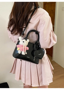 Detail of black shell bag with plush bear charm and heart pendant on shoulder strap