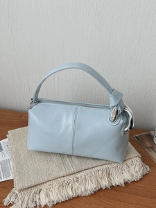 Light blue cylinder handbag with silver chain link handle on beige textured fabric