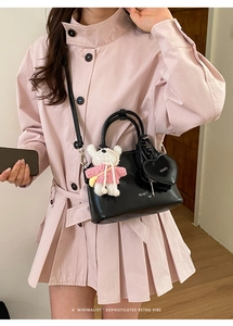 Detail of black shell crossbody bag with heart charm and white bear doll pendant