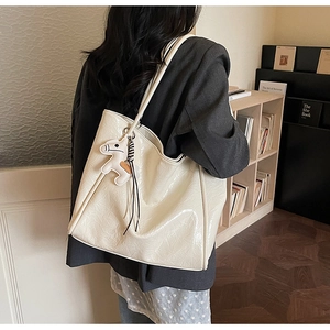 Detail of cream white tote bag with pleated texture and horse charm worn on shoulder