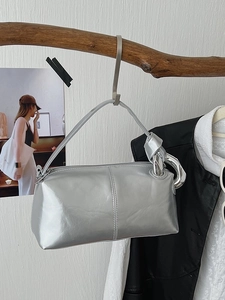 Minimalist silver metallic handbag with unique knot detail and large rings on a branch