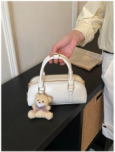 Detail of cream Boston bag with glossy wrinkled texture and teddy bear pendant