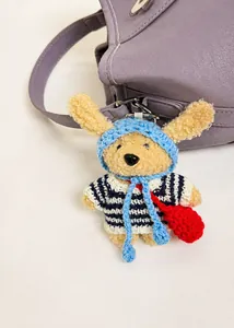 Close-up of a cute plush animal charm with a striped sweater on a purple leather bag