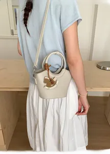 Detail der cremefarbenen Beuteltasche mit Litschi-Struktur und Schaukelpferd-Anhänger