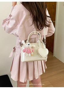 Detail of cream shell bag featuring plush rabbit charm and heart tag on a pink dress