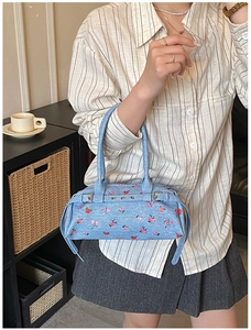 Close-up of light blue floral denim handbag featuring red flower prints and silver buckles