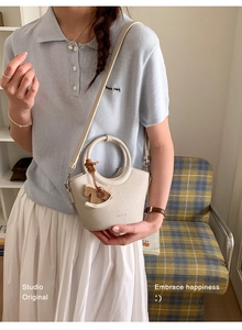 Schicke cremefarbene Leder-Eimertasche mit Rundgriff und Holzpferd-Anhänger am Model