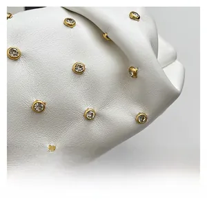 Close-up of white leather texture with gold-rimmed crystal rivets on the handbag