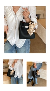Detail of black lychee grain leather bucket bag with metal lock and bear charm accessory