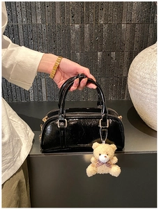Detail of black patent leather Boston bag with gold hardware and plush bear charm