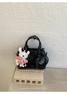 Detail of a minimalist black leather shell bag with heart charm and plush bear pendant