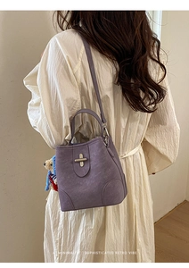 Detail of purple bucket bag with metallic twist lock and cute bear charm worn with beige dress