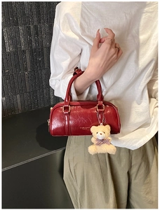 Detail of red glossy pleated Boston bag with cute beige teddy bear charm and gold hardware