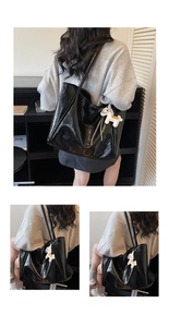 Close-up of black glossy pleated tote bag featuring a white pony leather charm accessory