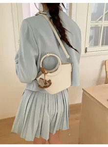 Model view of cream bucket bag with round handle and horse charm over blue dress