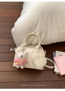 Detail of cream white shell handbag featuring heart charm and cute rabbit plush toy