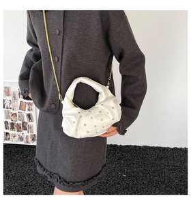 Detail of white pleated handbag featuring golden rivets and elegant metal chain strap