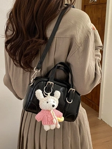 Minimalist black patent leather handbag with plush rabbit charm shown on model