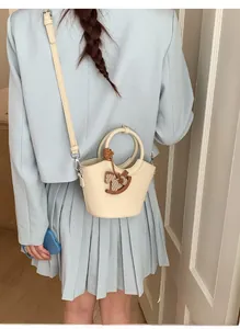 Detail der cremeweißen Leder-Eimertasche mit Tragegriff und hölzernem Pferdeanhänger
