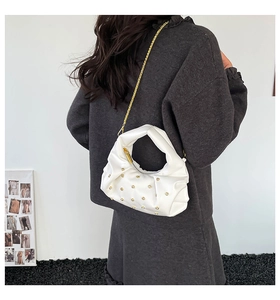 Detail of white pleated shoulder bag with gold studs and chain strap on a model