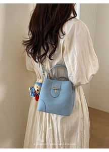 Detail of light blue bucket bag with gold clasp and teddy bear charm on model back