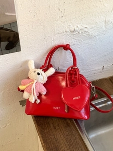 Red patent leather shell handbag with heart charm and white knitted animal mascot decoration