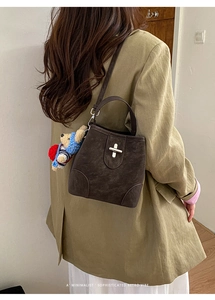 Detail view of dark brown suede bucket bag with silver twist lock and bear charm