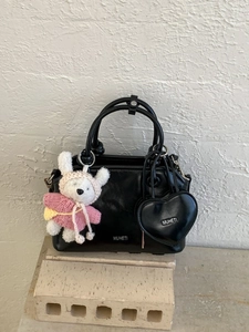 Elegant black shell-shaped handbag with plush charm and heart pendant on stone base