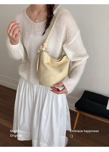 Detail of a cream bucket bag showing lychee grain texture and unique knotted shoulder strap