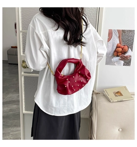 Detail of red pleated shoulder bag with gold rivets and chain strap on a model