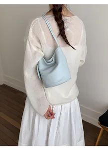 Detail of light blue lychee pattern leather bucket bag worn by model in minimalist setting