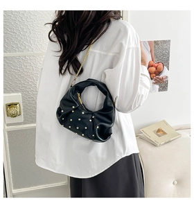 Detail of black pleated leather half-moon bag with gold rivets and chain strap