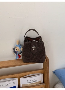 Detailed close-up of retro brown suede bucket bag featuring a cute teddy bear pendant