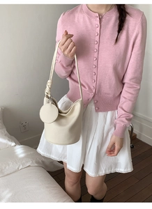 Detail of cream white bucket bag with round charm shown in minimalist fashion scene