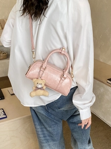 Pink patent leather cylinder bag with shiny texture and bear charm worn cross-body