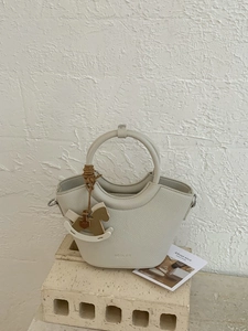 Minimalist cream white leather bucket bag with ring handle and rocking horse charm on stone