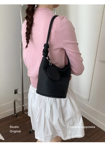 Detail of black leather bucket bag with knotted strap and circular charm decoration