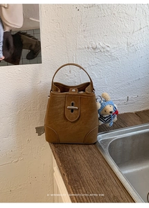 Detail of brown retro leather bucket bag with silver metal lock and teddy bear charm