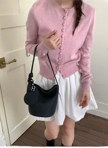 Minimalist black bucket bag shown as part of a stylish pink cardigan and white skirt outfit