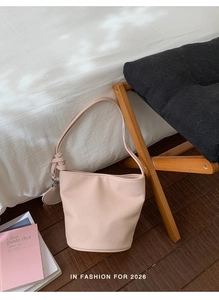 Detail of light pink bucket bag with leather texture and knotted decorative strap